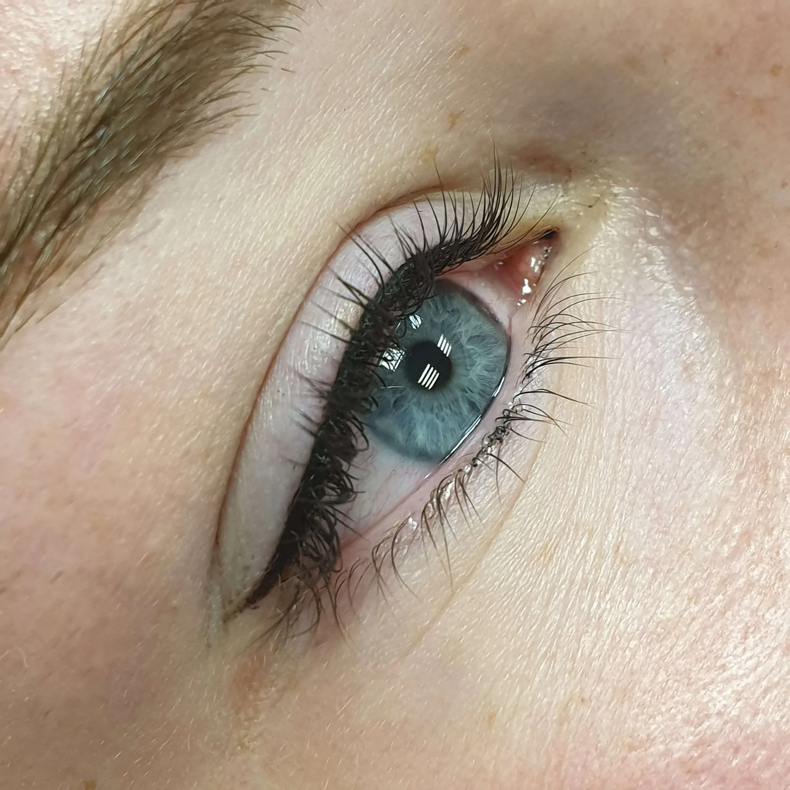 Winged permanent eyeliner on blue eyes, thickening the lash line to a fine point