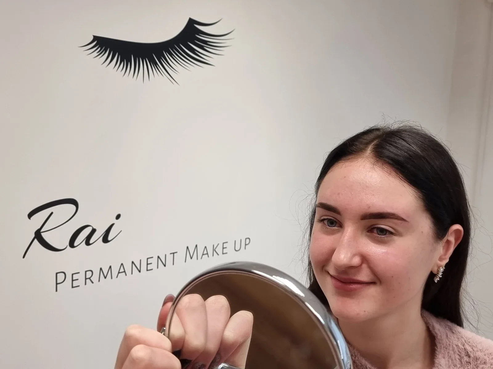 A client checking her brows in a hand mirror at the Rai Permanent Make Up studio